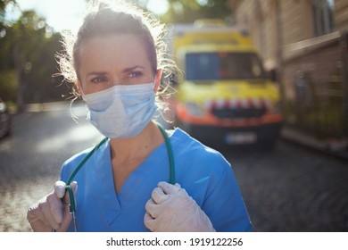 Covid-19 Pandemic. Pensive Modern Paramedic Woman In Uniform With Stethoscope And Medical Mask Outside Near Ambulance.