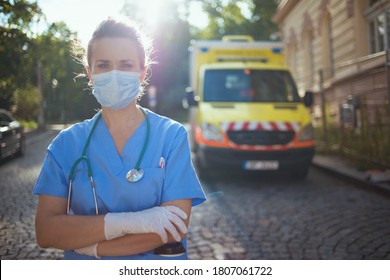 Covid-19 Pandemic. Portrait Of Modern Paramedic Woman In Uniform With Stethoscope And Medical Mask Outside Near Ambulance.