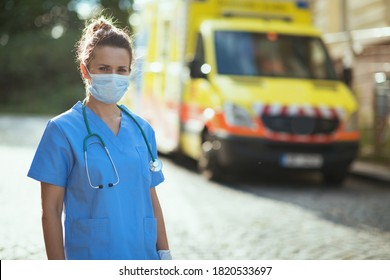 Covid-19 Pandemic. Portrait Of Modern Paramedic Woman In Uniform With Stethoscope And Medical Mask Outside Near Ambulance.