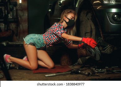 Covid-19 Pandemic Protection Concept. A Beautiful Young Girl With A Mask On Her Face Is Repairing A Car At A Service Station. Car Wheel Rim Repair. 