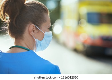 Covid-19 Pandemic. Seen From Behind Medical Doctor Woman In Uniform With Medical Mask Outside Near Ambulance.