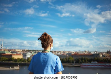 Covid-19 Pandemic. Seen From Behind Modern Medical Doctor Woman In Scrubs With Medical Mask Outside Against Sky.