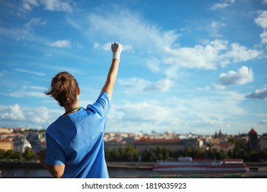 covid-19 pandemic. Seen from behind modern medical practitioner woman in scrubs with rubber gloves rejoicing outside in the city against sky. - Powered by Shutterstock