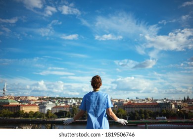 Covid-19 Pandemic. Seen From Behind Modern Physician Woman In Scrubs With Rubber Gloves Outdoors In The City Against Sky.