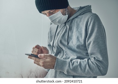 Covid-19 patient using smartphone for communication while being self-isolated in quarantine. Adult male standing by the window and typing text message.