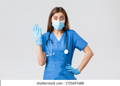 Covid-19, Preventing Virus, Health, Healthcare Workers And Quarantine Concept. Surprised Cute Female Nurse In Blue Scrubs Saying Hello, See Someone In Clinic, Wave Hi, Wear Medical Mask And Gloves