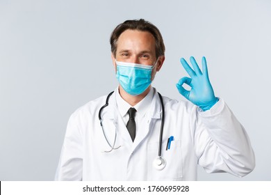 Covid-19, Preventing Virus, Healthcare And Vaccination Concept. Happy Smiling Doctor In Medical Mask And Gloves Assure All Good, Show Okay Sign As Guarantee Safety And Quality Of Service In Clinic