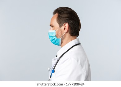 Covid-19, Preventing Virus, Healthcare Workers And Vaccination Concept. Profile Of Serious Determined Doctor In Medical Mask And White Coat Examine Patients, Looking Left Confident