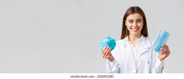 Covid-19, Preventing Virus, Healthcare Workers Concept. Smiling Attractive Female Doctor In White Scrubs Showing Two Variants Of Personal Protective Equipment, Show Respirator And Medical Mask