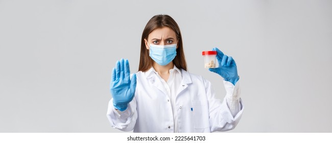 Covid-19, Preventing Virus, Healthcare Workers And Quarantine Concept. Serious Concerned Doctor In Medical Mask And PPE, Tell To Stop Using This Pills, Showing Bad Medicine Or Antibiotics.