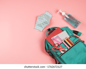 COVID-19 prevention while going back  to school  and new normal  concept.Top view of backpack with school supplies , blue polka dot fabric masks and sanitizer gel on pink background.