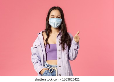 Covid19, quarantine, people concept. Happy confident young girl show thumbs-up while standing in medical face mask and look camera encourage stay safe during coronavirus outbreak - Powered by Shutterstock