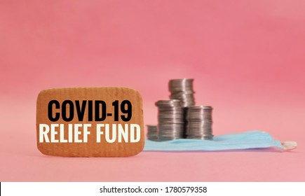 Covid-19 Relief Fund Note With Blurred Medical Face Mask And Stack Of Coins Money In Background