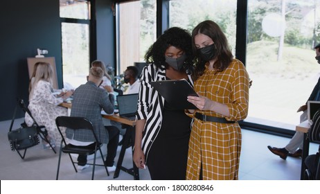 COVID-19 Safety At Workplace. Happy Young Multiethnic Female Colleagues Greet With Elbows Wearing Masks At Modern Office