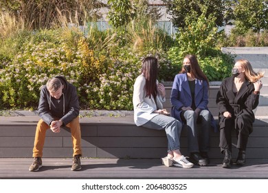 Covid-19, Social Distance Concept. Group Of Talking Women With Protective Face Masks And Man Without Face Mask Sitting In Distance During Pandemic Outbreak And Sunny Autumn Day. Image With Motion Blur