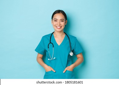 Covid-19, social distancing and coronavirus pandemic concept. Close-up of professional doctor, woman working as nurse or physician wearing scrubs, holding hands in pockets and smiling broadly