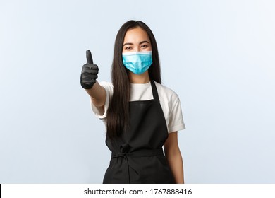 Covid-19, Social Distancing, Small Coffee Shop Business And Preventing Virus Concept. Smiling Asian Female Barista, Employee In Medical Mask And Gloves Show Thumb-up