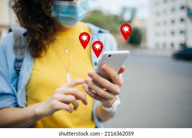 COVID-19 Tracking App Concept With Geolocation Icons Pop Up. Woman Wearing Protective Face Mask Holding Smartphone With Coronavirus Tracing Software On City Street