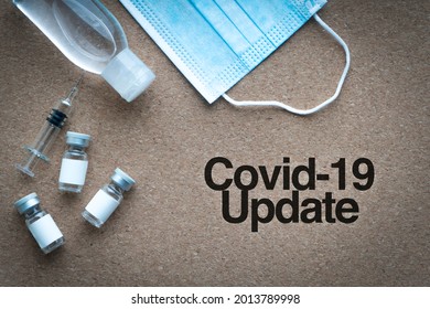 COVID-19 UPDATE Text With Face Mask, Hand Sanitizer, Syringe And Vials On Wooden Background. Covid-19, Business And Copy Space Concept

