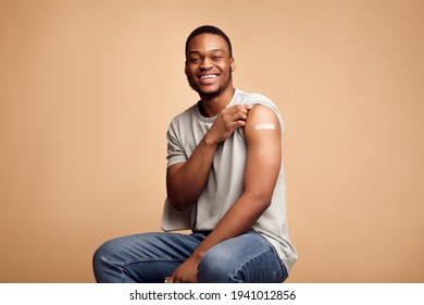 Covid-19 Vaccinated African Man Showing Arm With Plaster, Beige Background