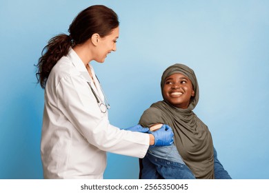 Covid-19 Vaccination. Black Muslim Female Patient Getting Vaccinated Against Coronavirus, Nurse Applying Adhesive Bandage Plaster On Vaccinated Arm After Vaccine Injection On Blue Studio Background - Powered by Shutterstock