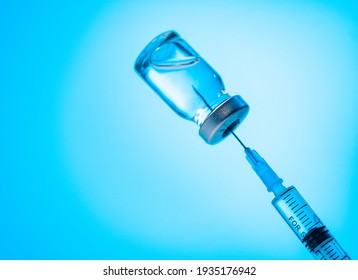 COVID-19 vaccination campaign. Filling of syringe with coronavirus vaccine from vial, close up in neon blue light