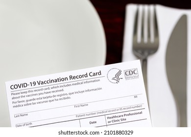 Covid-19 vaccination card and restaurant table. Indoor vaccine mandate, entertainment restrictions and vaccination requirement concept. - Shutterstock ID 2101880329