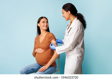 Covid-19 Vaccination. Pregnant Female Patient Getting Vaccinated Against Coronavirus, Medical Worker Applying Plaster Bandage On Vaccinated Arm Over Blue Studio Background - Powered by Shutterstock