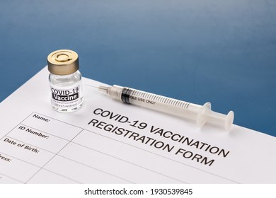 Covid-19 Vaccination Registration Form With Vial And Syringe As Prop On Blue Desk