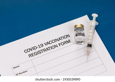 Covid-19 Vaccination Registration Form With Vial And Syringe As Prop On Blue Desk