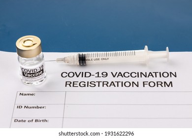 Covid-19 Vaccination Registration Form With Vial And Syringe As Prop On Blue Desk