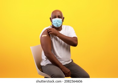Covid-19 Vaccination. Senior Black Man In Medical Mask Showing Band Aid After Getting Coronavirus Vaccine Shot On Orange Studio Background. Vaccinated Elderly Patient Receiving Anti Covid Injection