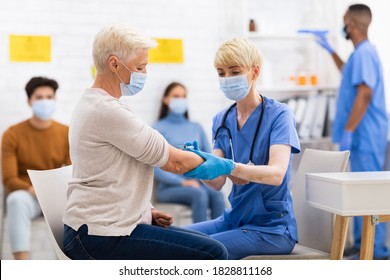 Covid-19 Vaccination. Senior Patient Lady Getting Vaccinated Against Coronavirus Sitting With Doctor In Hospital, Wearing Face Mask. Nurse Injecting Corona Virus Vaccine Shot To Older Woman
