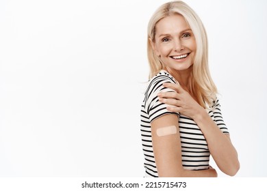 Covid-19 Vaccination. Smiling Senior Woman Shows Band Aid After Covid-19 Vaccine Shot, Looking Happy, Standing Over White Background