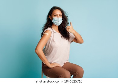 Covid-19 Vaccination. Vaccinated Woman Gesturing Thumbs Up Showing Arm With Plaster Bandage After Coronavirus Vaccine Injection On Blue Background, Wearing Protective Face Mask. Antivital Immunization - Powered by Shutterstock