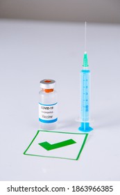 Covid-19 Vaccine Bottle And Syringe Next To It On A White Background With Sign Of Approval. Covid Vaccine Approval And Global Pandemic Concept.