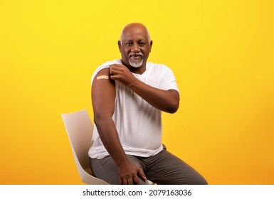 Covid-19 vaccine. Positive senior black man showing bandage on shoulder after coronavirus vaccination, orange studio background. Elderly male patient with band aid smiling at camera