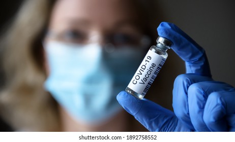 COVID-19 Vaccine In Scientist Hand Close-up, Female Doctor And Bottle With Medication For Coronavirus Cure In Lab. Concept Of Corona Virus Research, Vaccination And Clinical Trial During Pandemic.