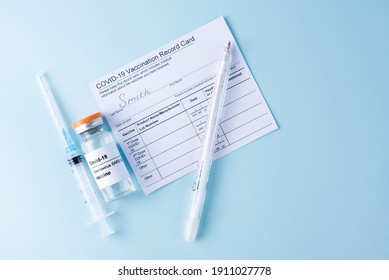 Covid-19 Vaccine Vial, Vaccination Record Card, Syringe, A Pen On A Blue Background, Copy Space, Close Up. Coronavirus Vaccination Concept.