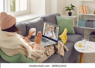 Covid-19 Virus, Flu Or Common Cold Consultation Via Online Medical Video Chat. Sick Woman Wrapped In Blankets Sitting On Sofa At Home, Making Skype Call To EHealth Doctor And Waving Hand At Laptop