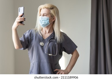 Covid19, Virus, Health And Medicine Concept. Young Nurse In Medical Mask Taking Selfie On Smartphone, Videocalling Friends While Social Distancing