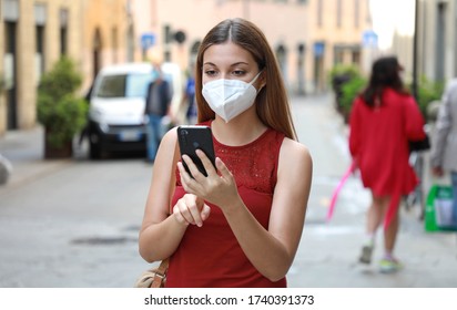 COVID-19 Woman In City Street Wearing KN95 FFP2 Mask Against Disease Virus SARS-CoV-2 And Using Smart Phone App To Aid Contact Tracing And Self Diagnostic In Response To Coronavirus Disease 2019