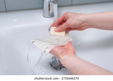 COVID-19 A Woman Washes A Reusable Cloth Face Mask With Her Hands In The Sink After Wearing At Office, Public Places, Transport. Homemade Cotton Mouth Mask That Can Be Washed In The Washing Machine.