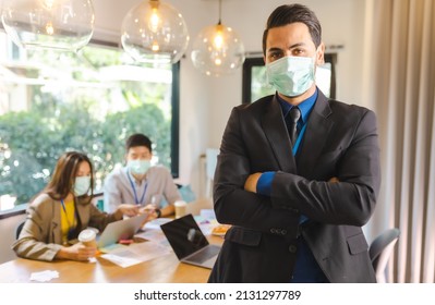 Covid-19. Young People With Face Masks Back At Work In Office After Lockdown.Asian Small Business Startup Multiracial Brainstorm Meeting With Laptop And Everyone Mask For Covid19 Protection Corona.