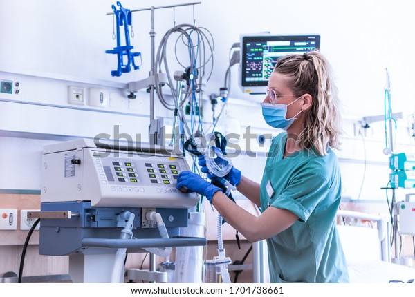 COVID19/2019-ncov concept: nurse, wearing a surgical\
mask, checks the settings of a mechanical ventilation machine,\
which is seen in the foreground. therapy used for lung breathing,\
in intensive\
care
