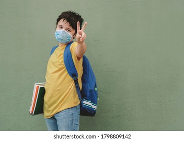 Covid-19,kid With Medical Mask And Backpack Going To School Doing Victory Sign Over Green Background