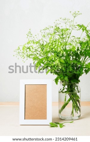 Cow parsley flowers in a glass jar and an empty picture frame on the table.