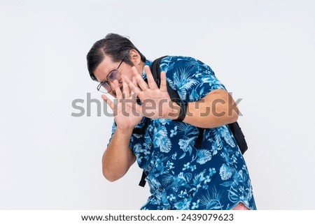 Cowardly middle-aged tourist in a Hawaiian shirt with a scared expression asking someone to stop, isolated on white.