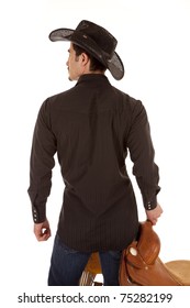 A Cowboy From The Back.  He Is Holding A Saddle.