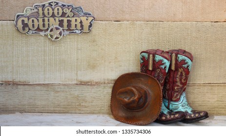 Cowboy boots, hat and 100% country sign on a wood background 